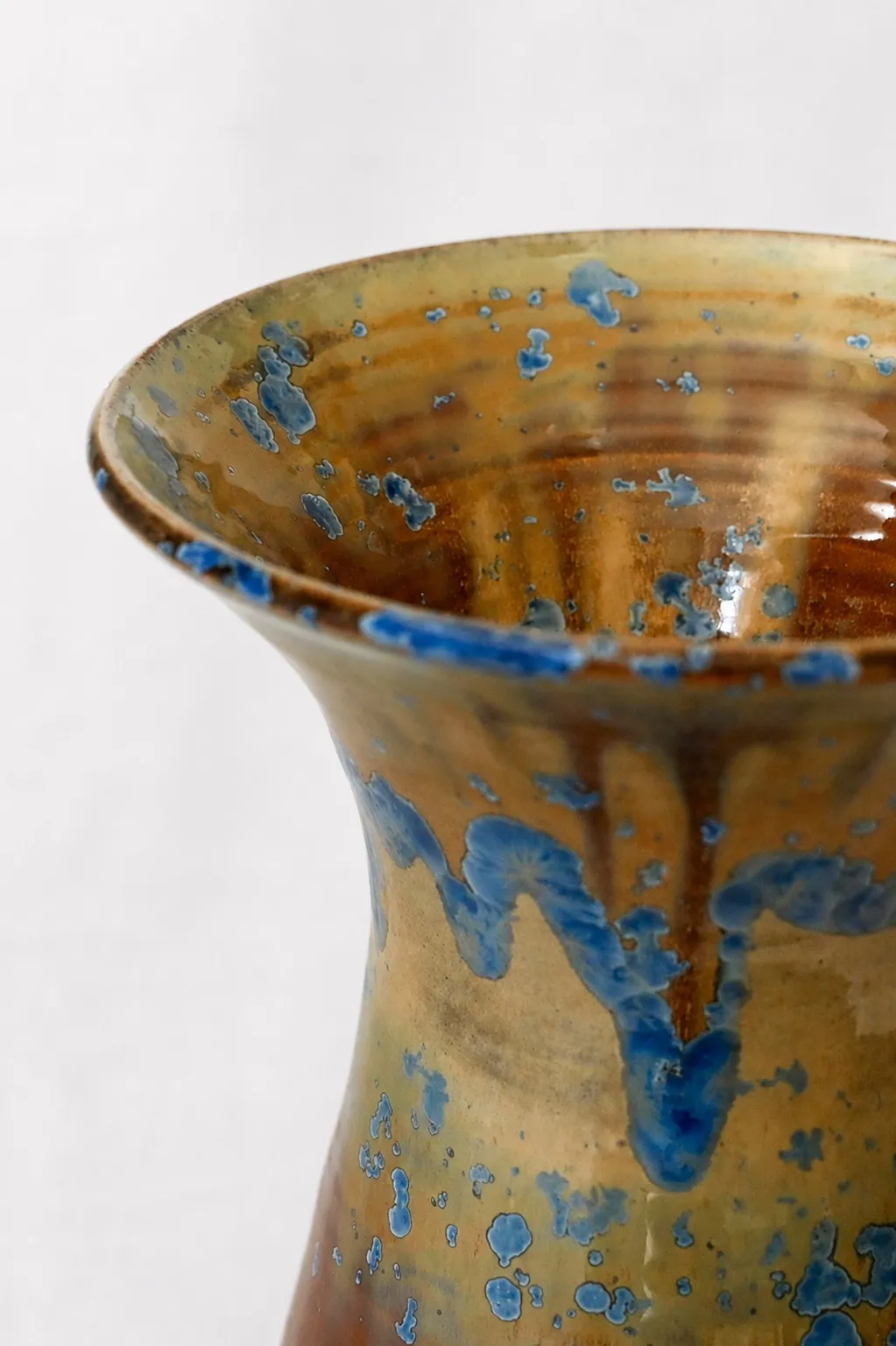 Close view of the flared neck and rim, blue crystals dripping over the amber glaze