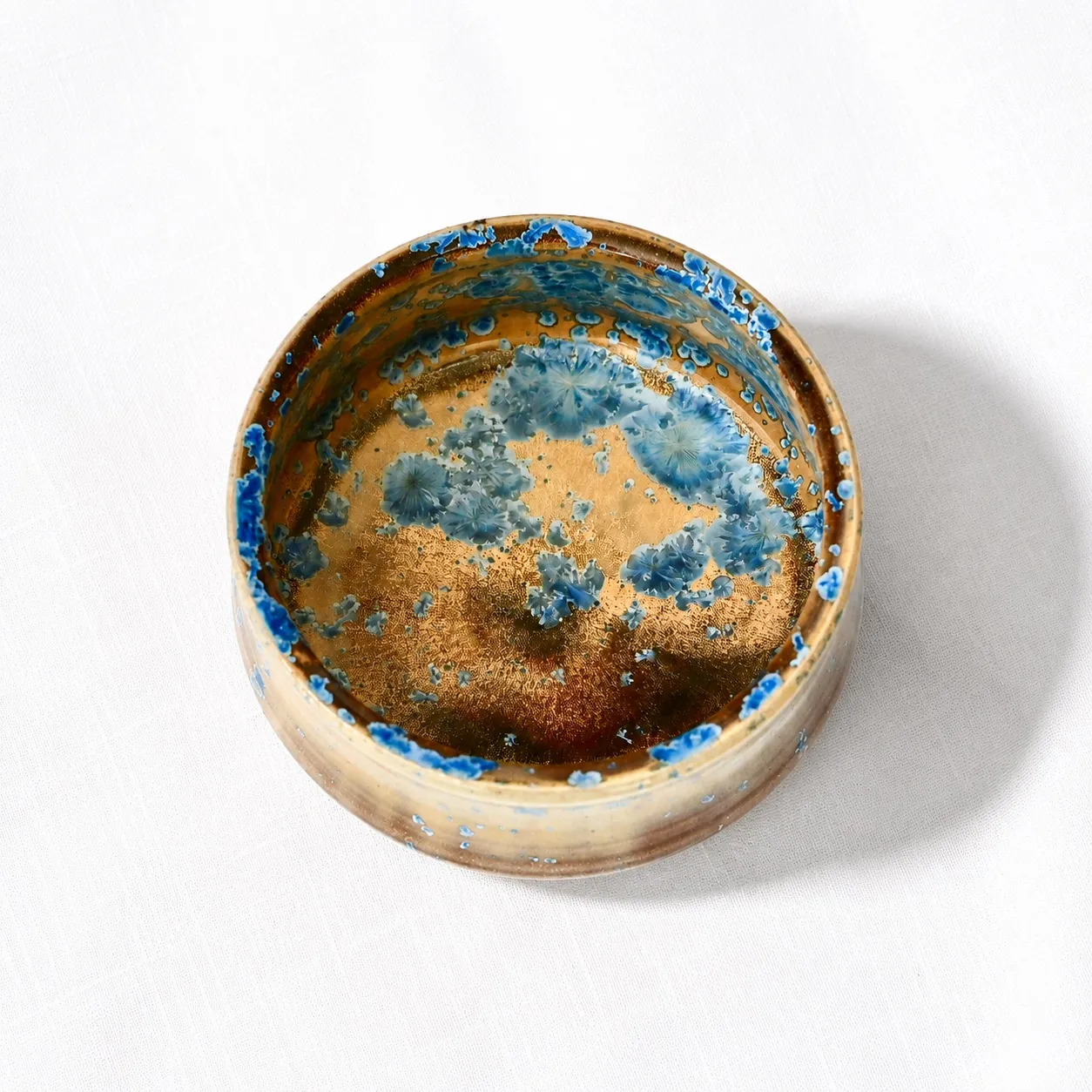 Looking down into a low stoneware bowl, blue crystals pooling and scattering across the ochre interior
