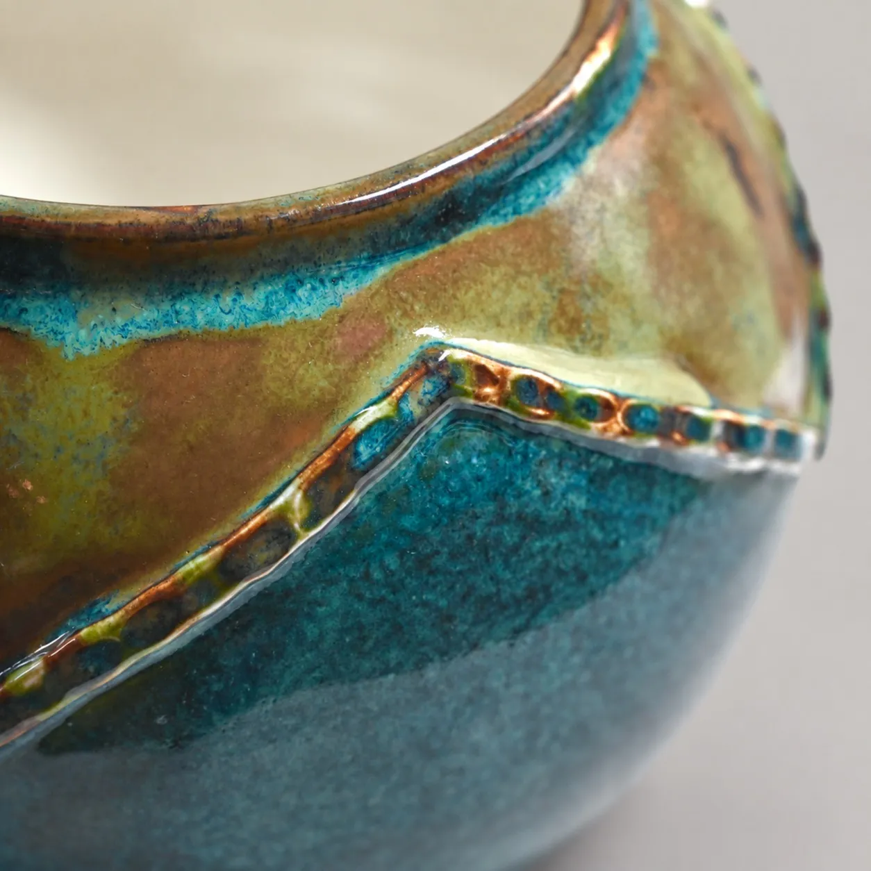 Close view of the rim, the amber glaze breaking to teal along a beaded zigzag seam