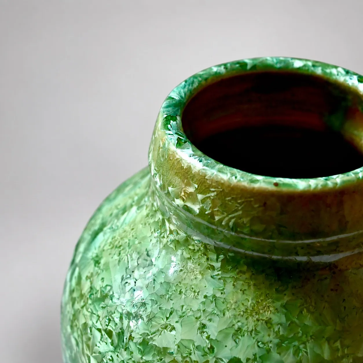 Close view of the rolled rim and shoulder, dense green crystal blooms over an amber ground