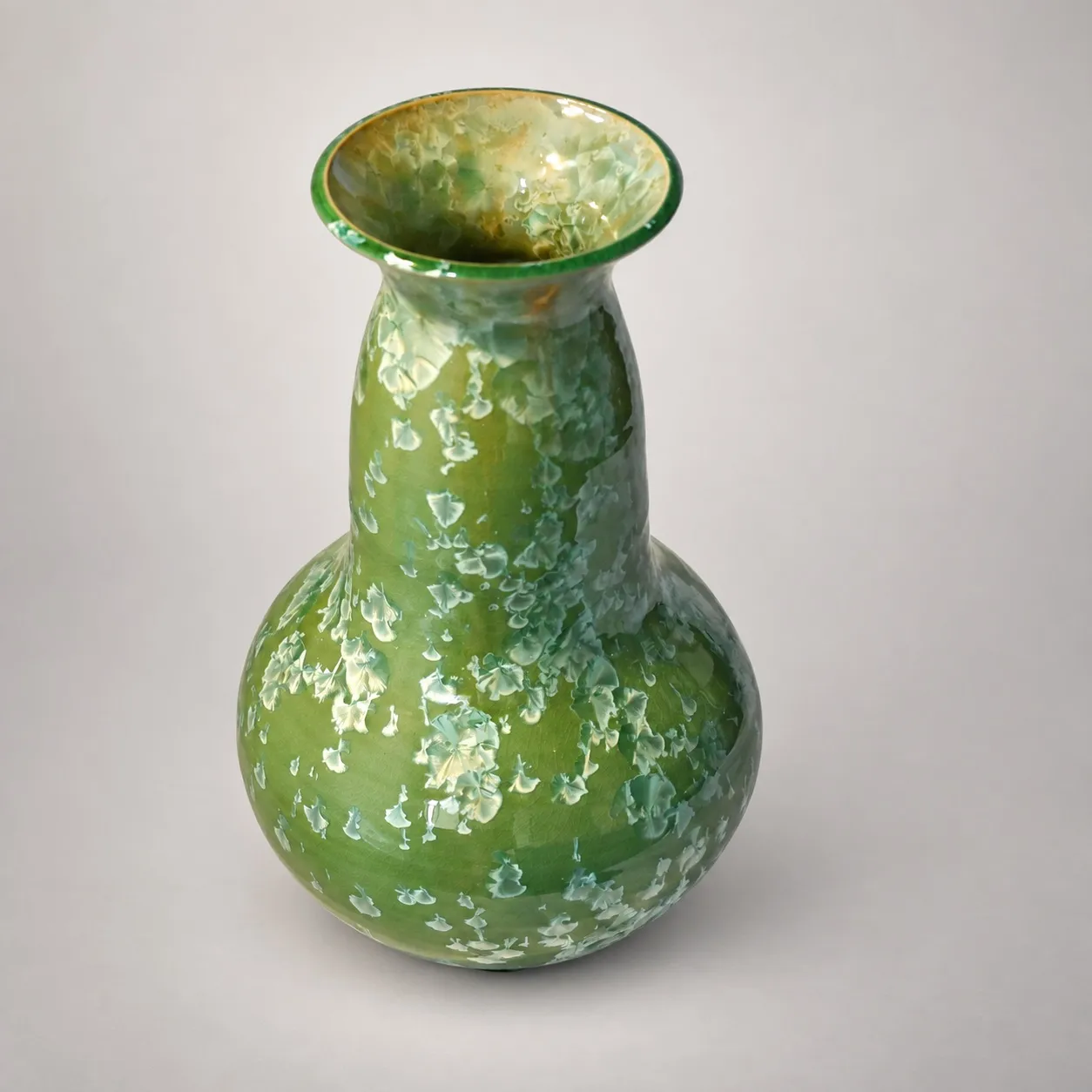A large gourd-shaped stoneware vase, bulbous below and drawn up to a tall neck and flared rim, bright green crystalline glaze scattered with pale mint and cream crystal blooms
