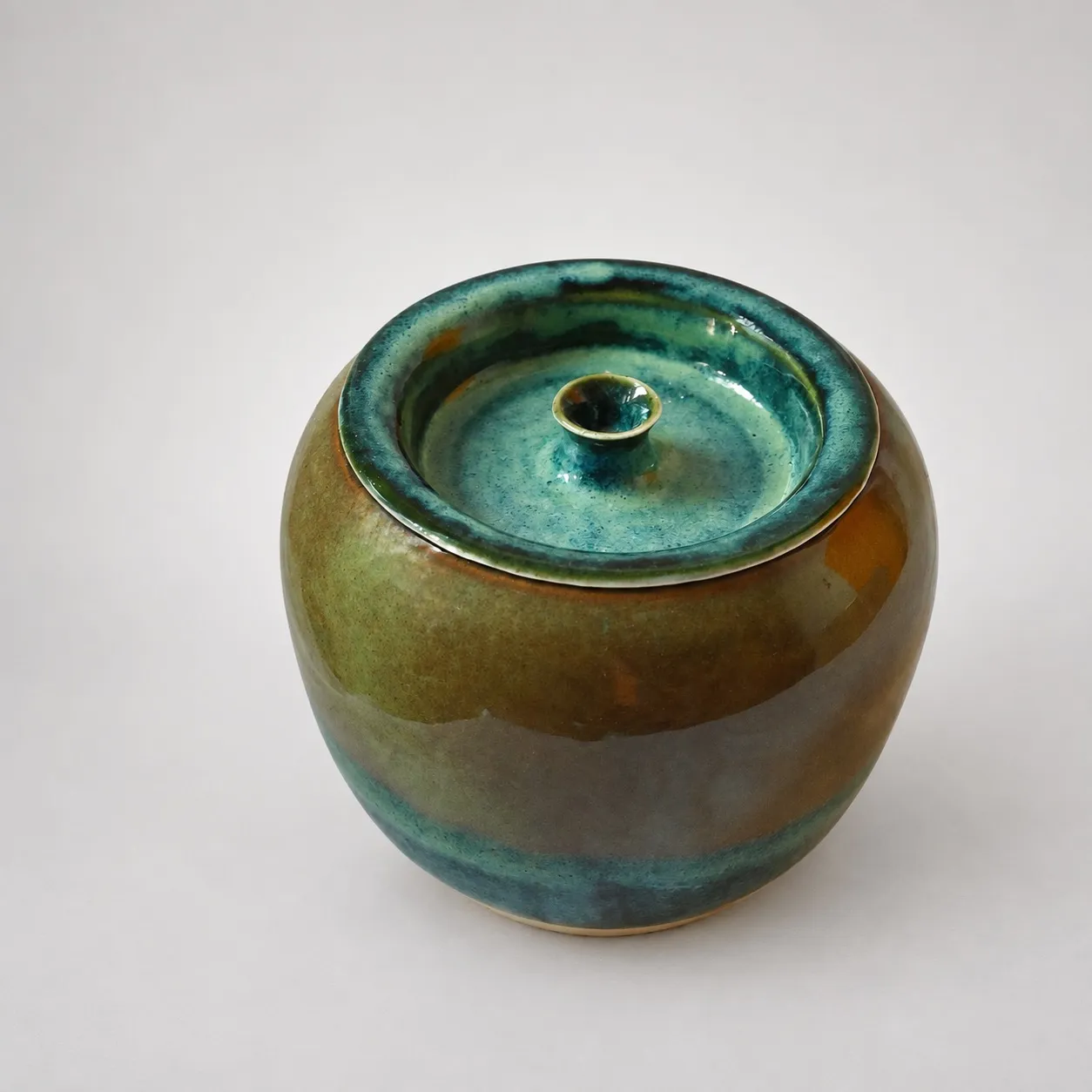 The jar from above with its lid seated, a teal-blue glazed lid and small knob ringed by the amber body