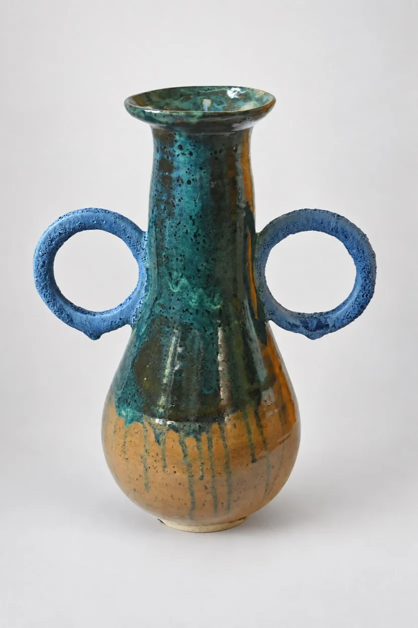 A tall two-handled stoneware bottle, volcanic teal-green glaze over the neck and shoulder running to amber below with blue drips, and two rough pale-blue ring handles