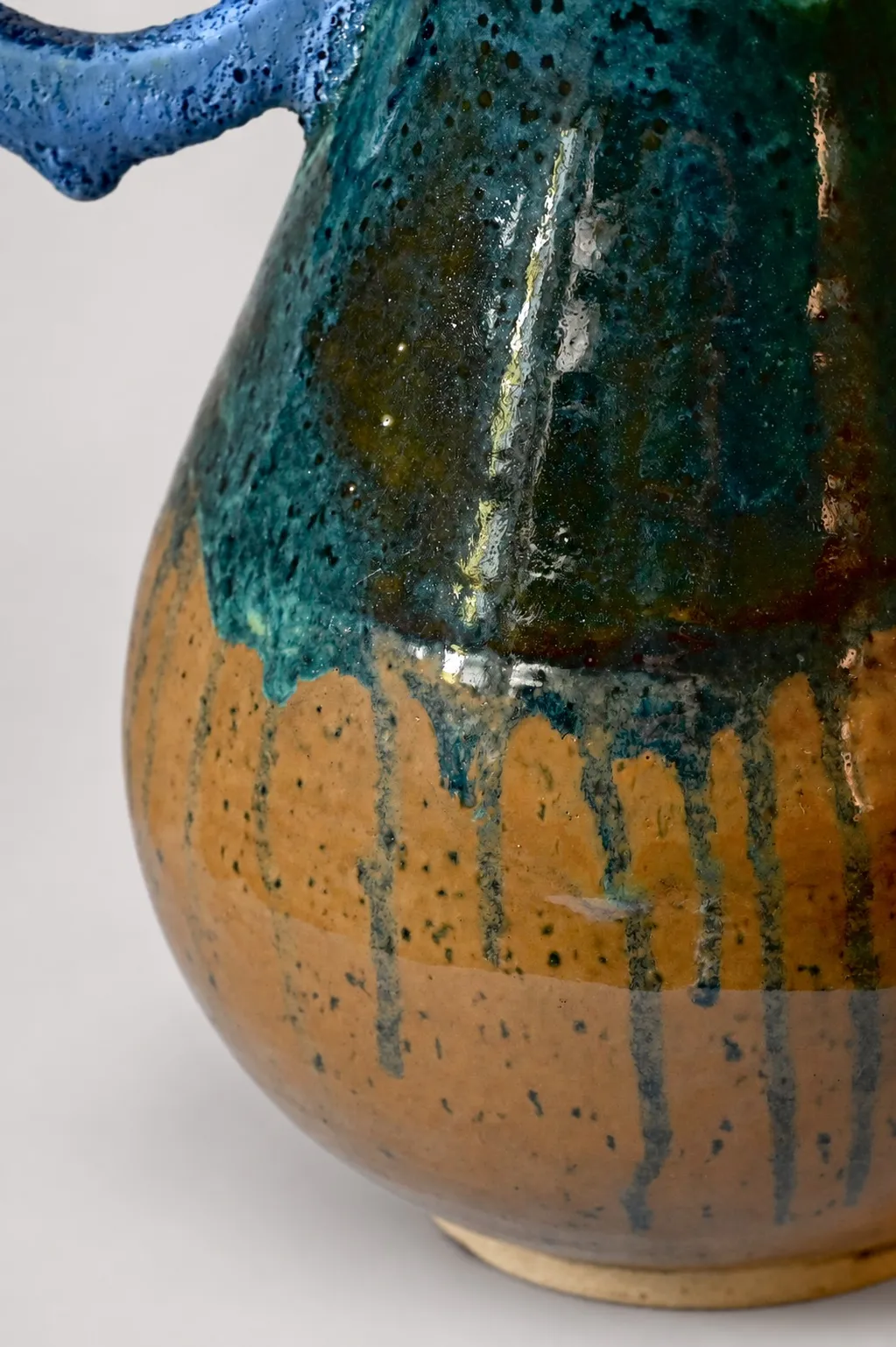 Close view of the lower body, teal glaze breaking to amber ochre with cobalt drips running down to the foot