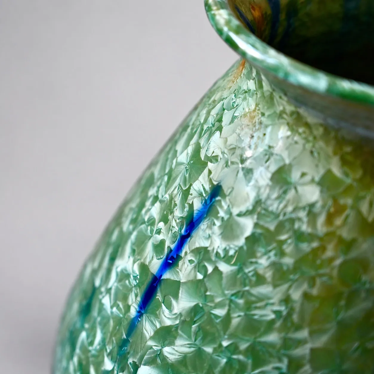 Close view of the shoulder, packed green crystal blooms crossed by a single vivid cobalt streak