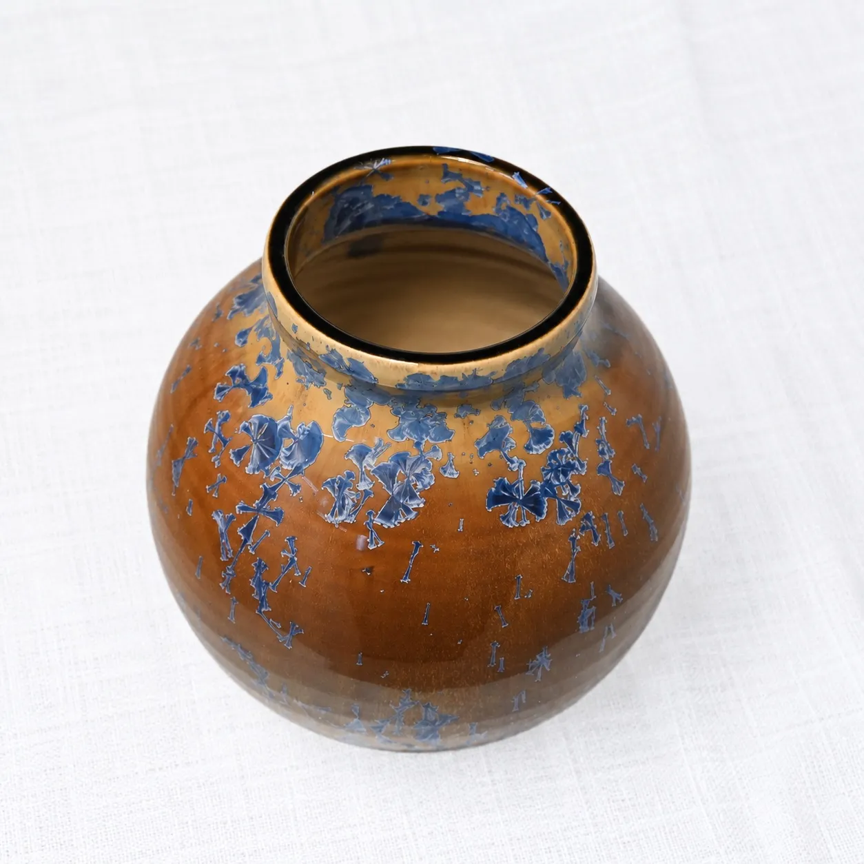 A round amber-brown stoneware vase with a short dark collar, blue crystal blooms gathered near the shoulder