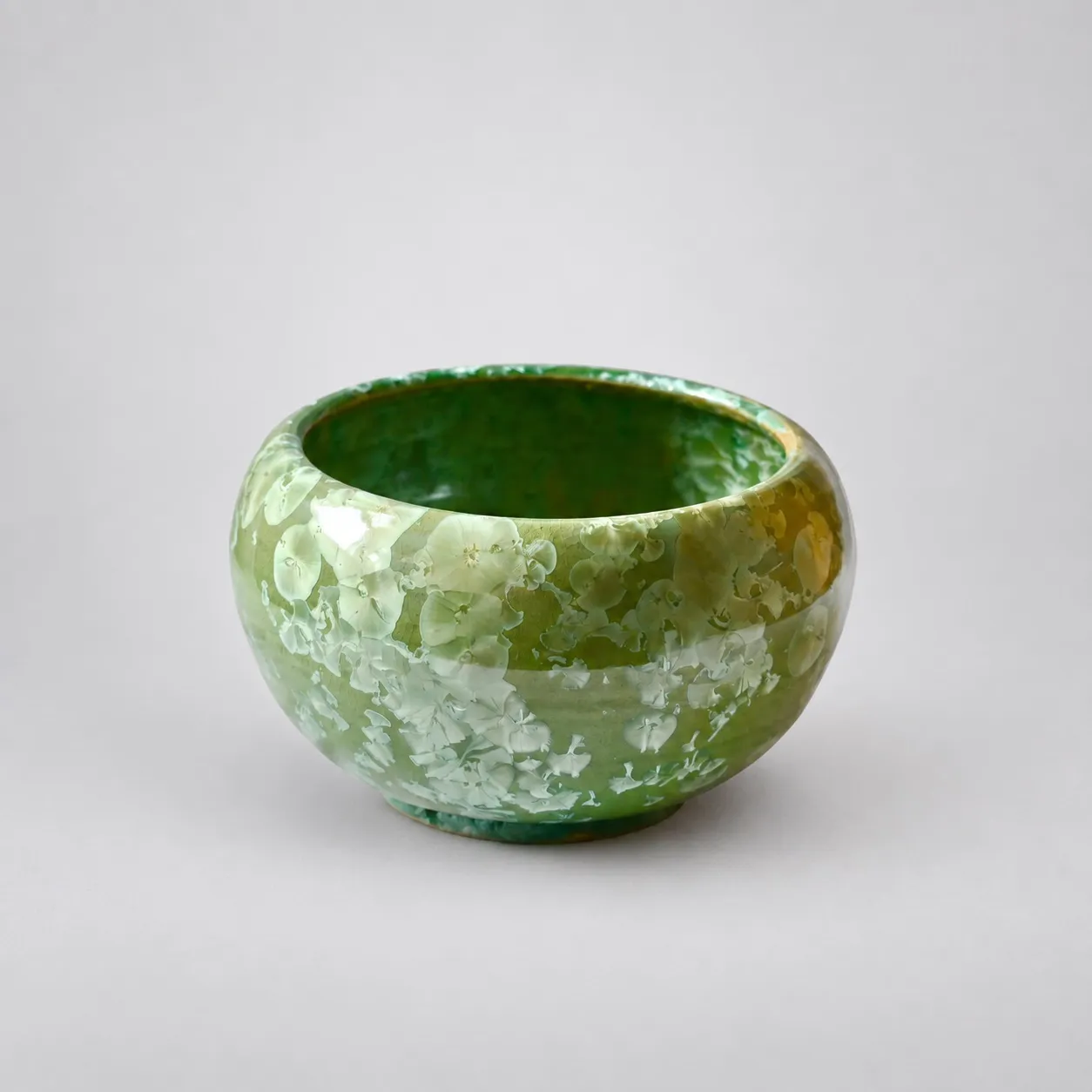 A low rounded stoneware bowl, green crystalline glaze with large pale crystal blooms and amber pooling toward the foot