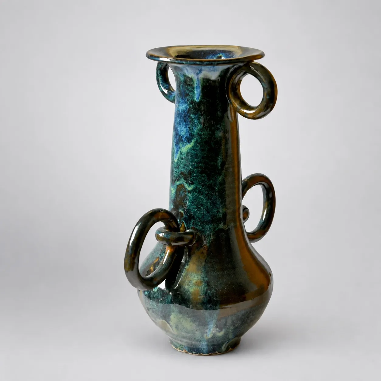 A tall stoneware vase with a bulbous base and long neck, glossy blue-green rutile glaze breaking to amber, hung with several ring handles passing through lugs