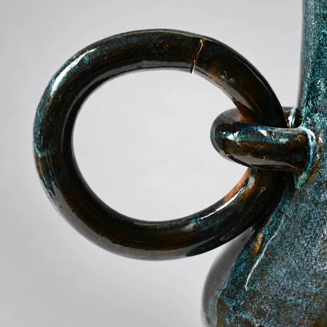 Close view of a ring hanging through its lug, glossy blue-black glaze with amber breaks, and a crack running clean through the upper part of the ring