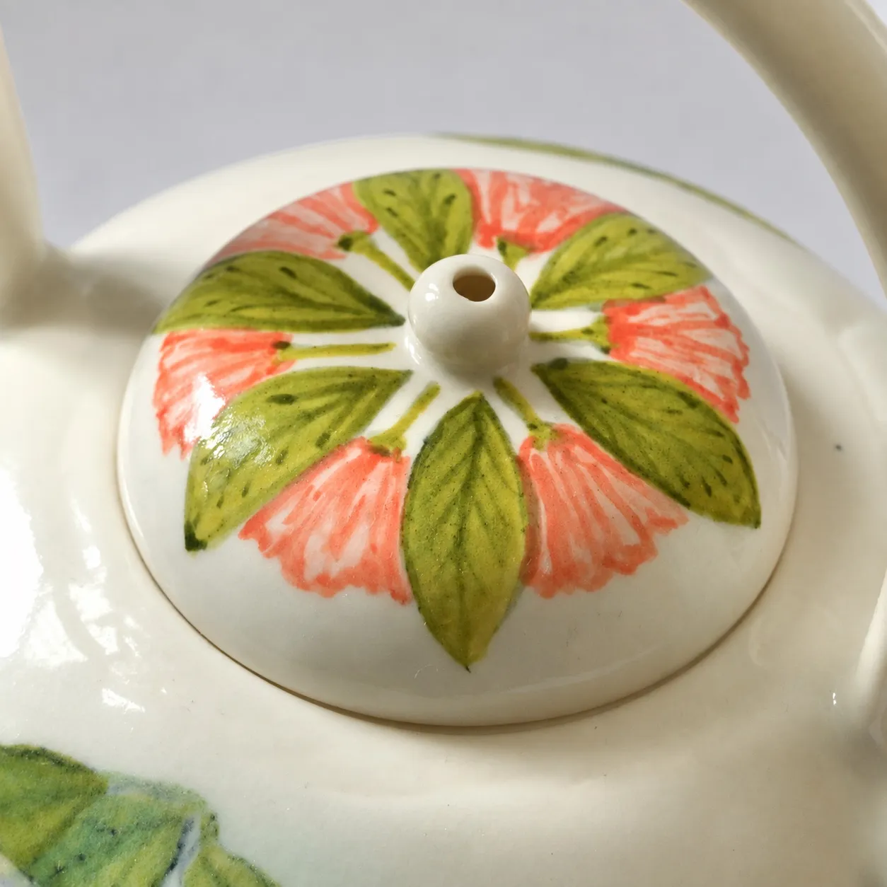 Close view of the domed lid, hand-painted with green leaves and coral petals radiating from the knob