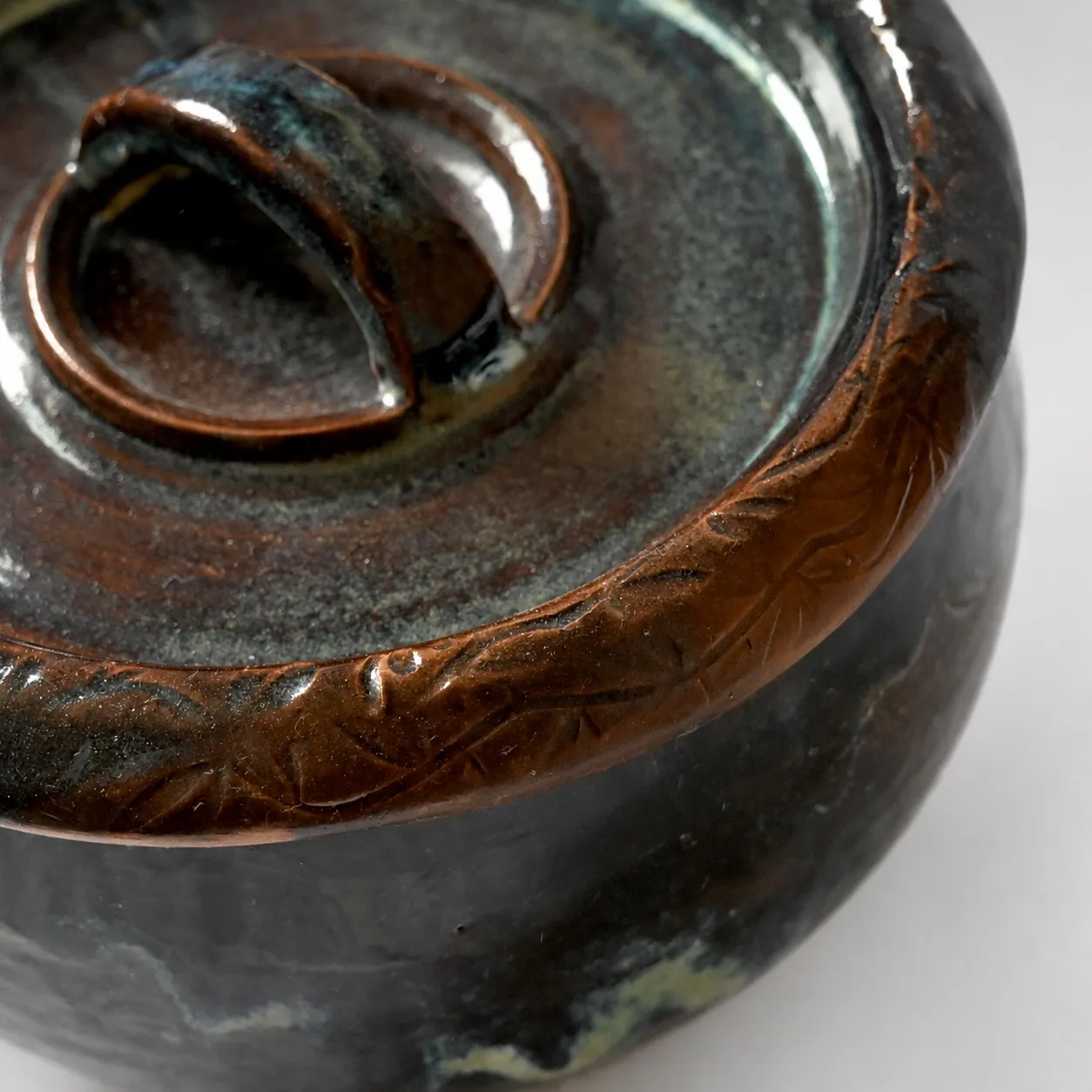 Close view of the lid, its looped knob and the carved band around the rim, amber breaking over deep blue