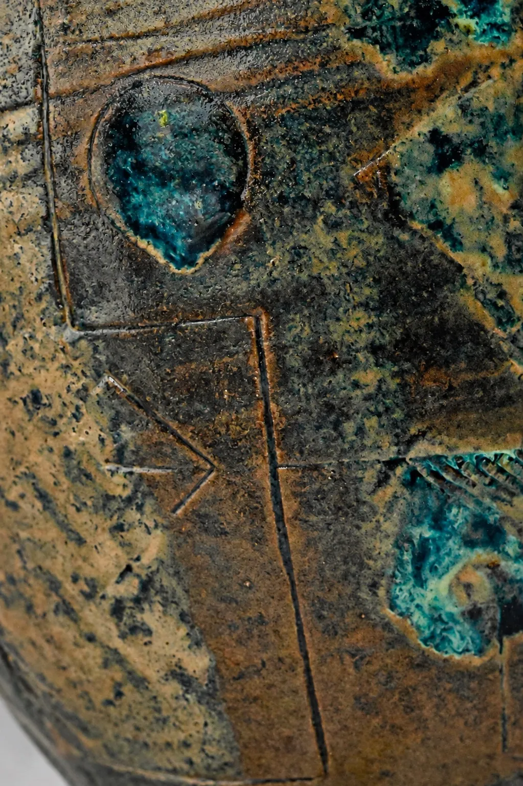 Close view of the incised surface, turquoise pooling inside a scratched circle and an arrow, against ochre breaking to near-black