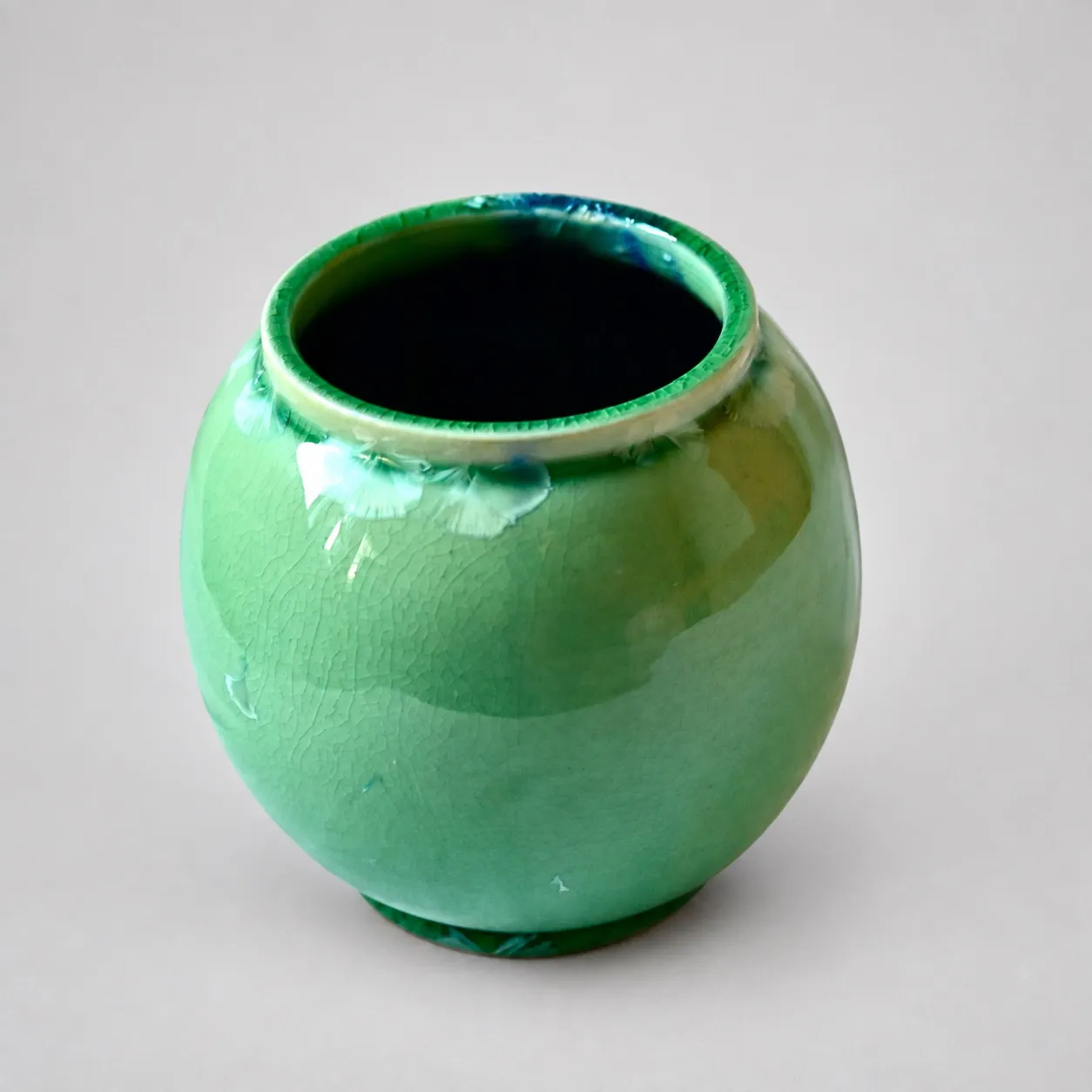 A small round porcelain pot in bright green crystalline glaze, fine crazing across the whole body and a ring of pale crystal fans around the shoulder just below the rim
