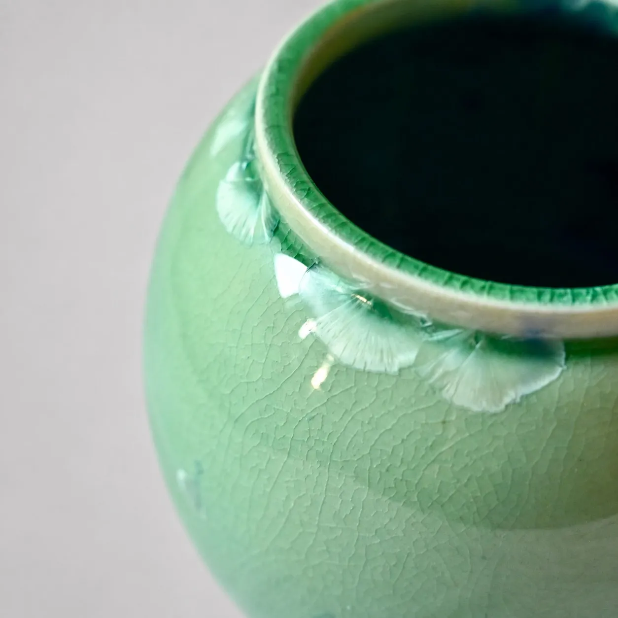Close view of the shoulder, pale crystal fans opening in a row below the rim, with fine crazing spreading across the green glaze below them