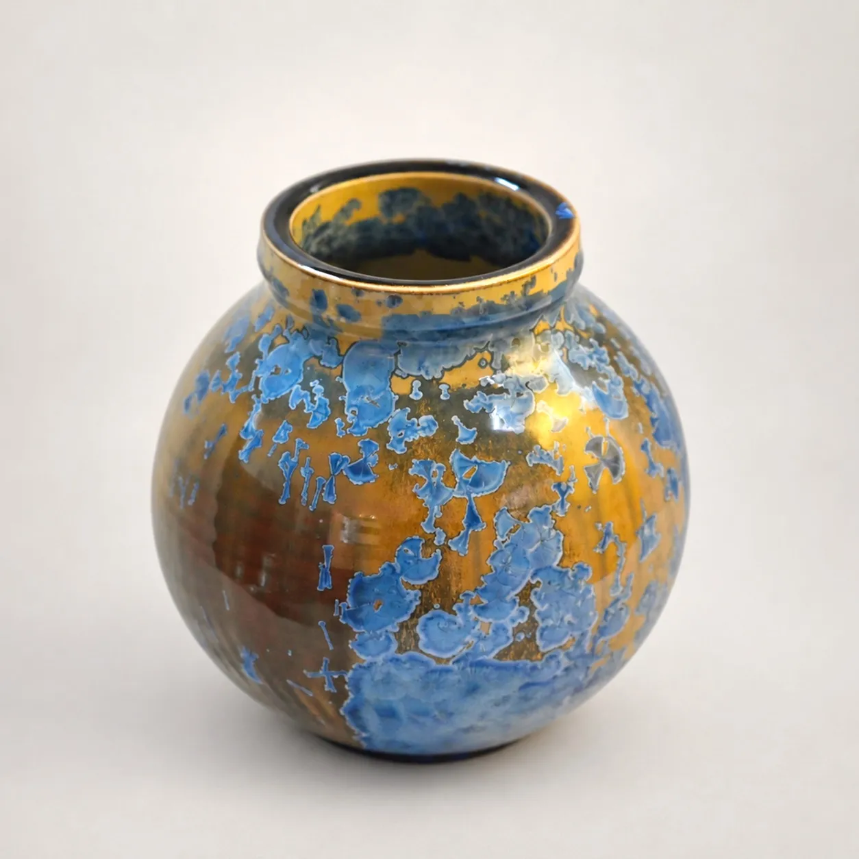 A round amber stoneware vase with a short flared neck, medium-blue crystal blooms scattered evenly over the body