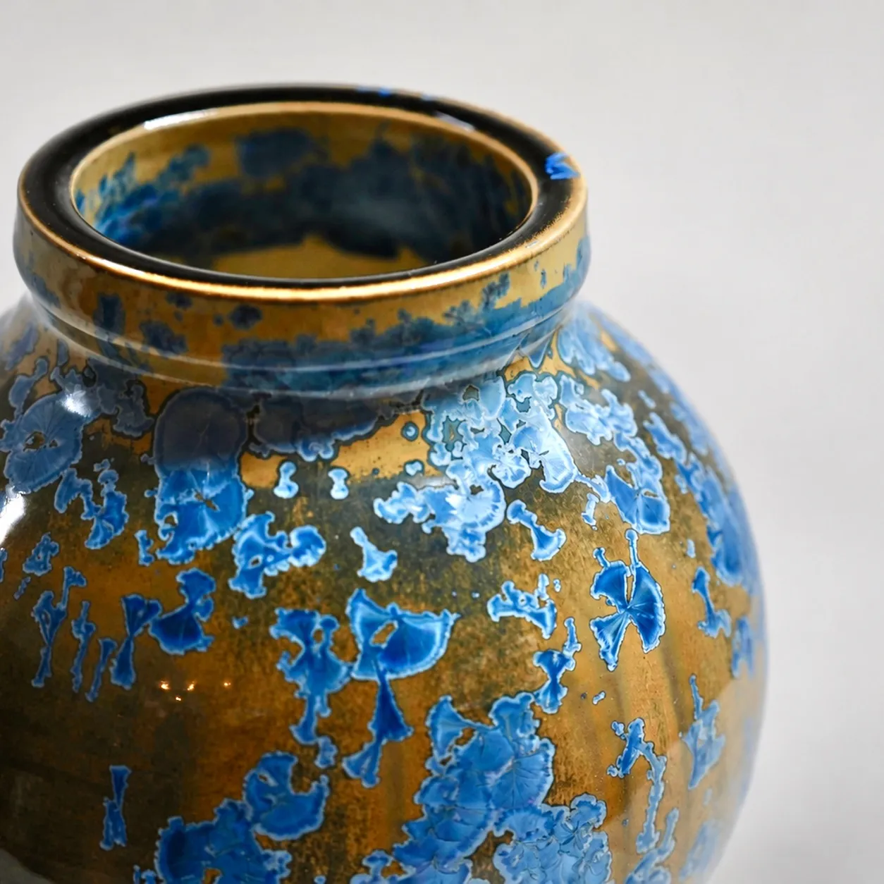 Close view of the rim and shoulder, blue crystals blooming densely across the amber glaze
