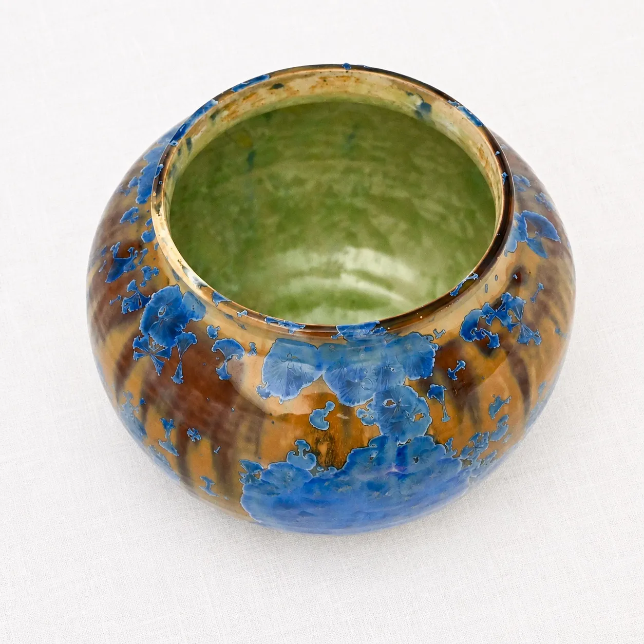 A squat round stoneware bowl, amber-and-blue crystalline outside with a glossy green interior