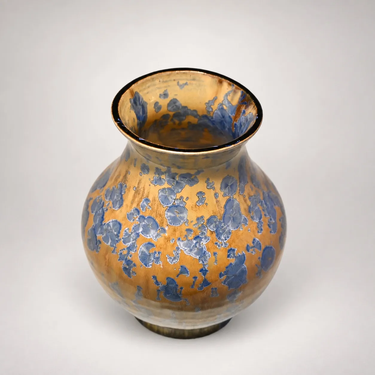 A rounded stoneware vase with a flared rim, pale beige ground scattered with slate-blue crystal blooms