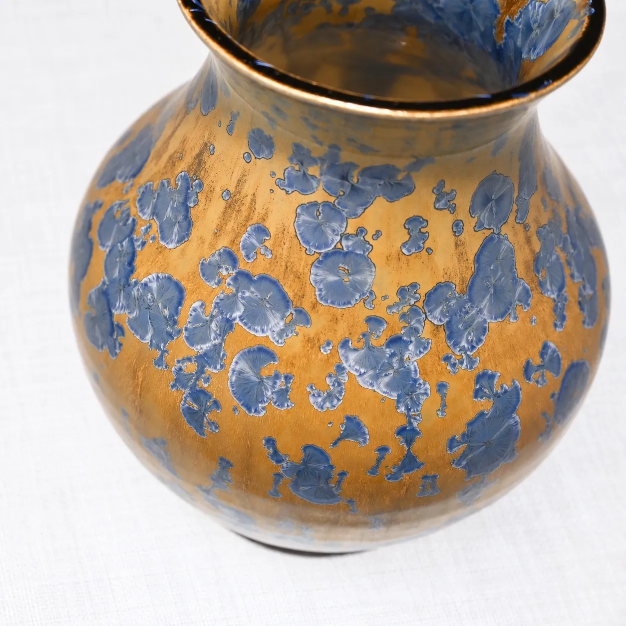 Close view of the glaze, blue crystals opening like pressed flowers across a warm beige ground
