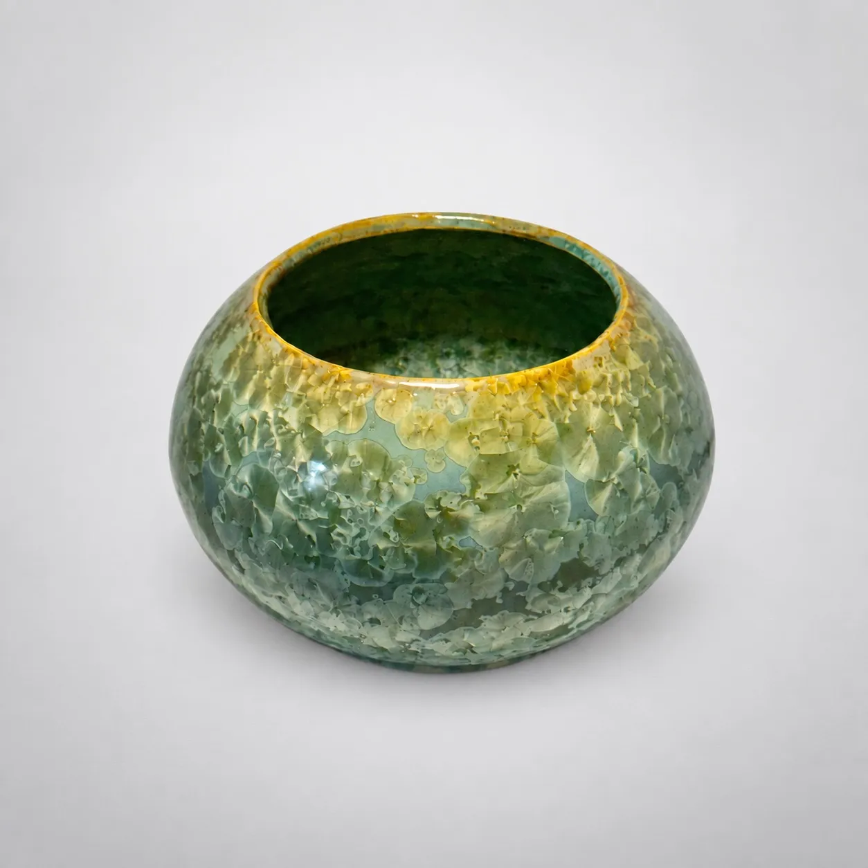 A rounded low stoneware bowl, sea-green glaze with a warm ochre rim and dense crystal growth