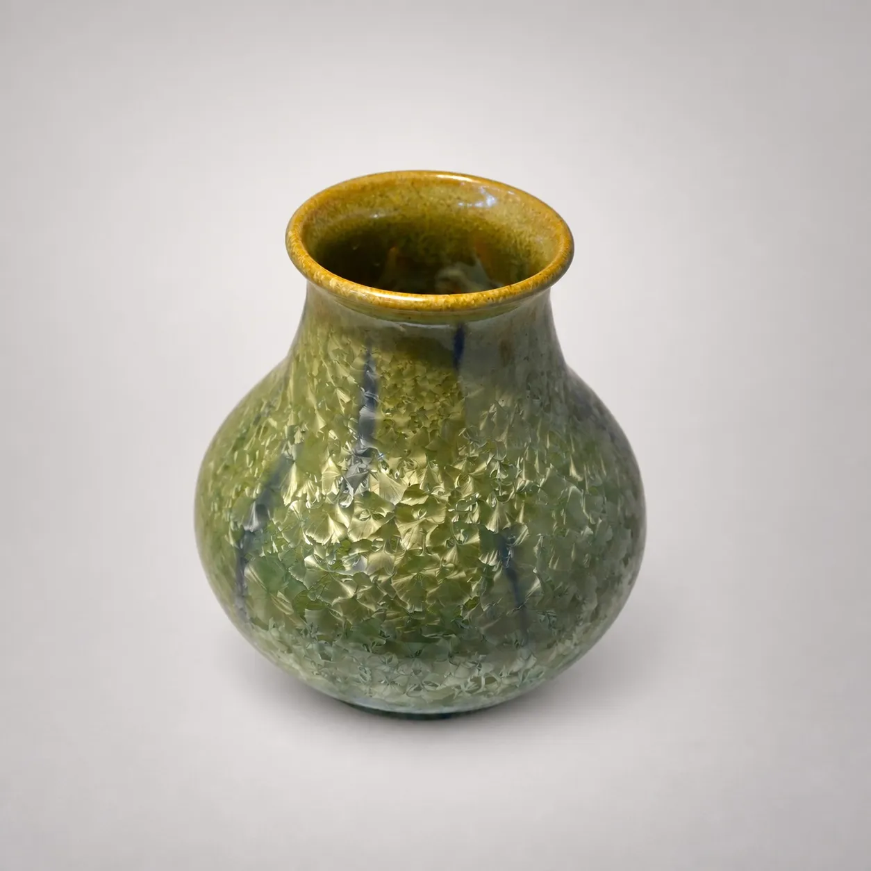 A small stoneware vase with a bulbous body and flared ochre rim, green crystals streaked with cobalt