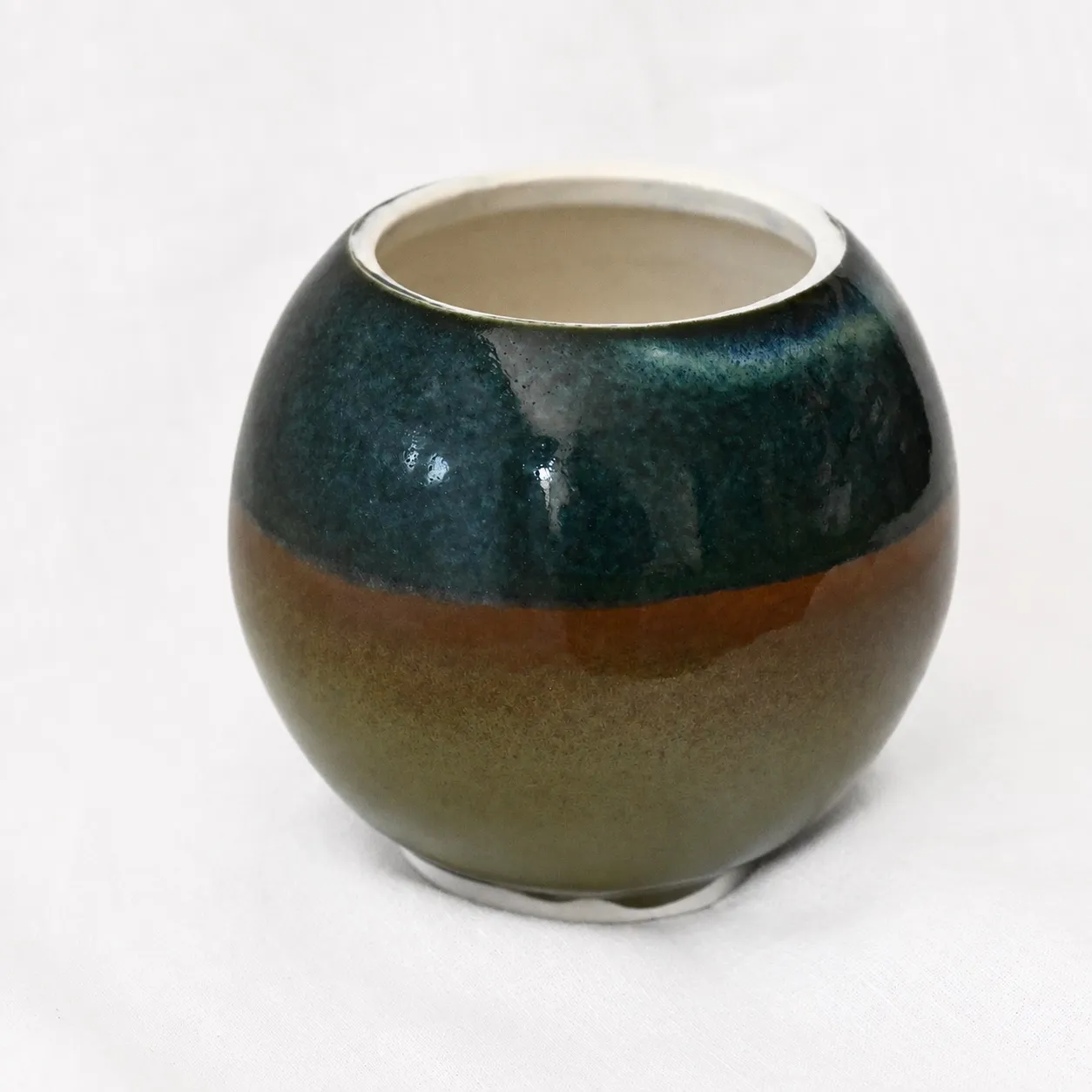 A small round porcelain pot, glossy blue-green banding over amber, with a white porcelain rim
