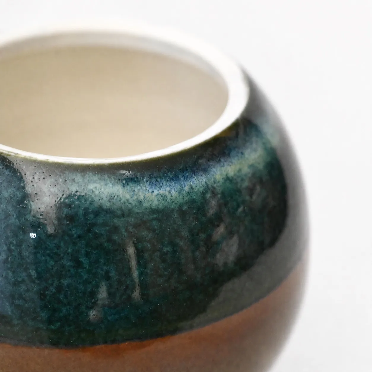 Close view of the rim, glossy blue-green glaze breaking to amber over the white porcelain lip