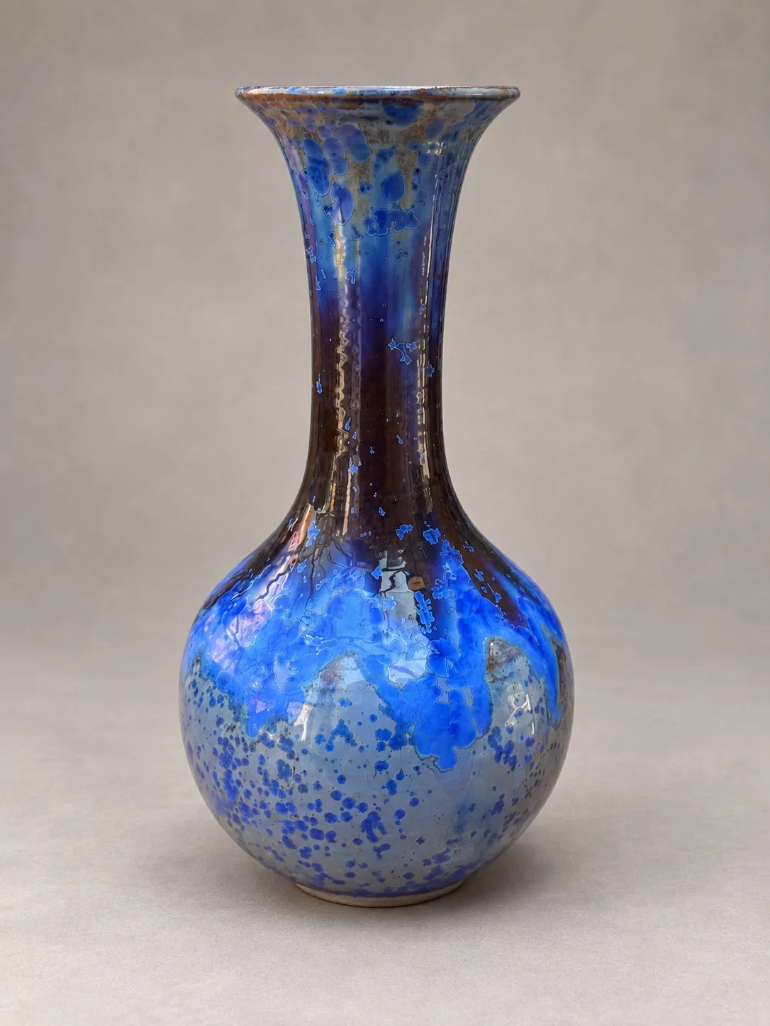 A stoneware vase by Igor Krol: a round body sitting low, a long neck rising from it and opening to a wide trumpet mouth, in deep blue scattered with brighter blue blooms.