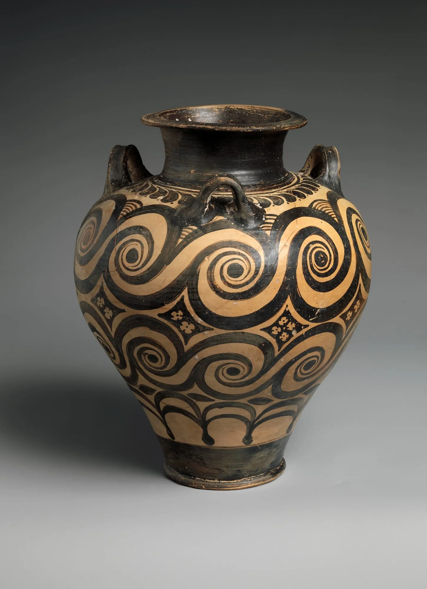 A Minoan jar: a continuously swelling body tapering to a small foot, a flaring collar, three small handles at the shoulder, painted all over with large black running spirals on cream.